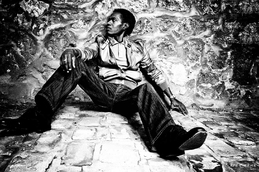homme noir assis contre un mur en pierre